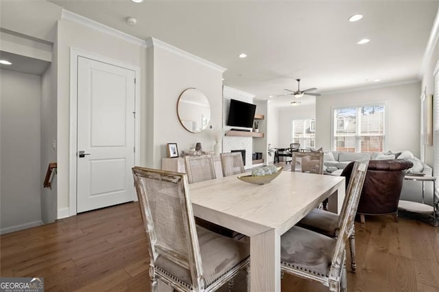 dining room with wood finished floors, ornamental molding, recessed lighting, ceiling fan, and a stone fireplace