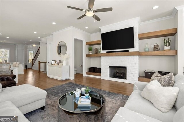 living area featuring wood finished floors, a brick fireplace, ceiling fan, ornamental molding, and recessed lighting