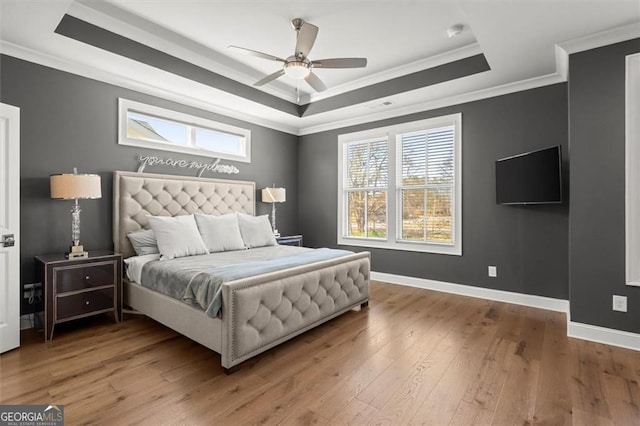 bedroom with a tray ceiling, crown molding, wood finished floors, and baseboards