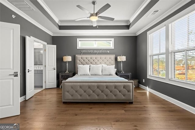 bedroom with multiple windows, a tray ceiling, and wood-type flooring