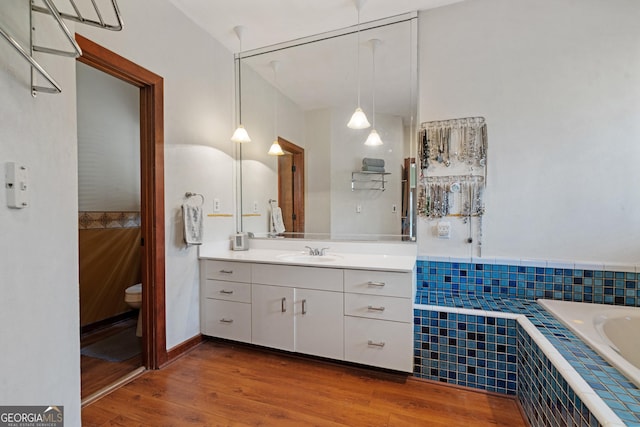 full bathroom with toilet, tiled bath, wood finished floors, and vanity