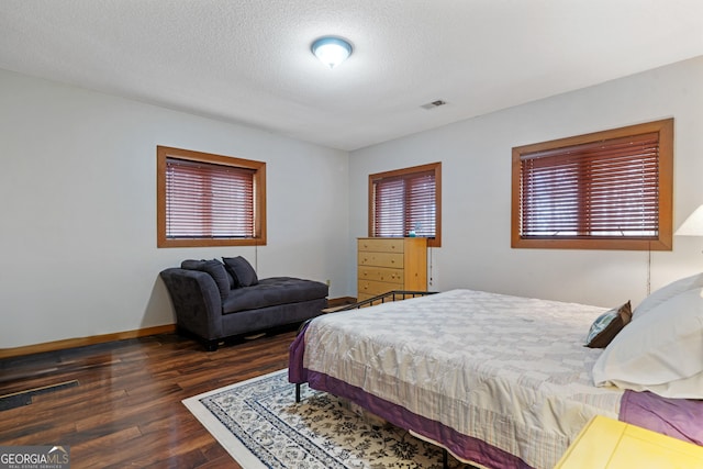 bedroom with baseboards, visible vents, wood finished floors, and a textured ceiling