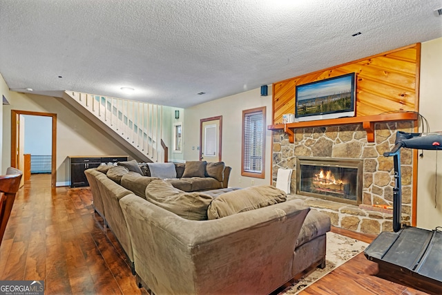 living room with hardwood / wood-style floors, a stone fireplace, stairs, and a textured ceiling