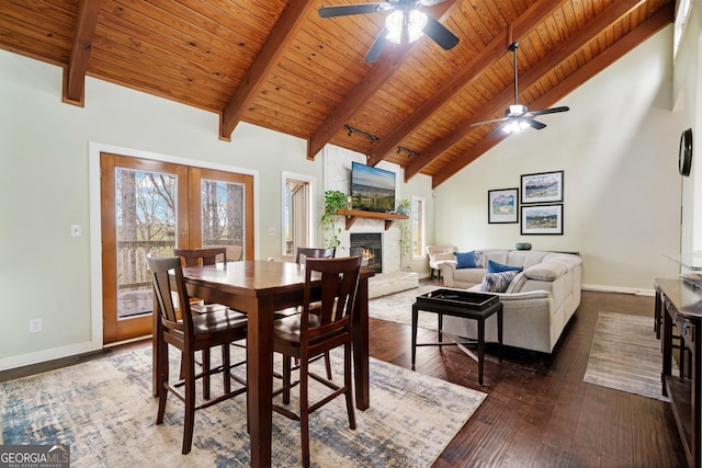dining room with high vaulted ceiling, beam ceiling, a ceiling fan, a stone fireplace, and baseboards
