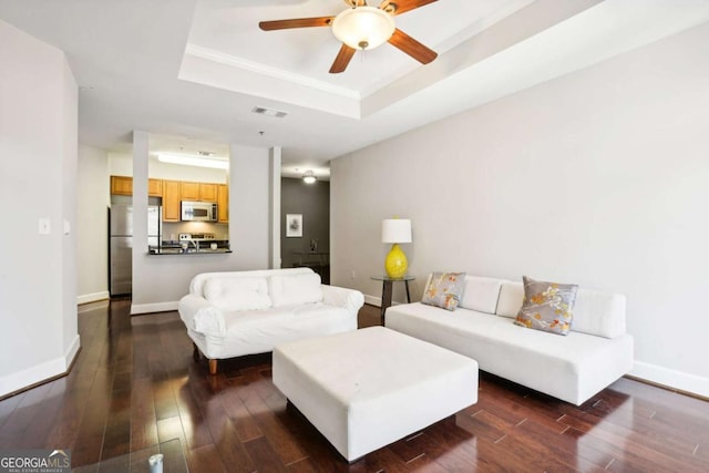 living room with hardwood / wood-style floors, a ceiling fan, a tray ceiling, and baseboards