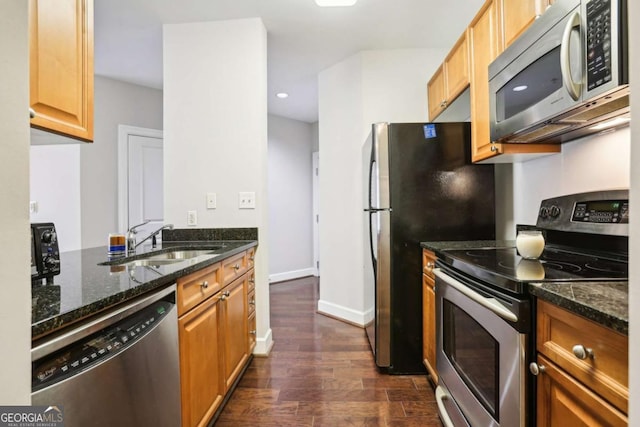 kitchen with a sink, stainless steel appliances, baseboards, dark wood-type flooring, and dark stone counters