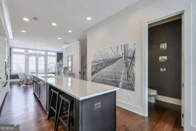 kitchen with light countertops, dark wood-style flooring, a sink, visible vents, and a kitchen island with sink