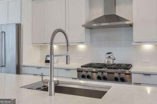 kitchen featuring stainless steel appliances, backsplash, a sink, wall chimney range hood, and white cabinets