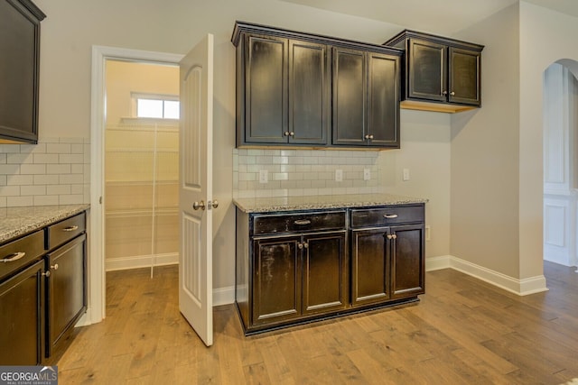 kitchen with baseboards, arched walkways, light wood finished floors, light stone countertops, and decorative backsplash