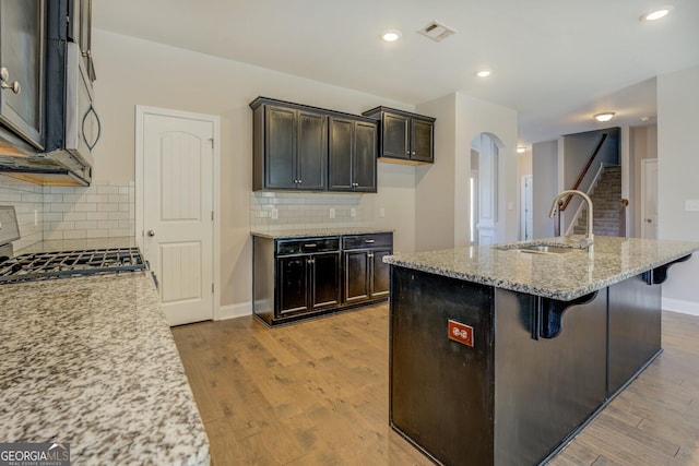 kitchen with visible vents, arched walkways, a sink, light wood-type flooring, and light stone counters