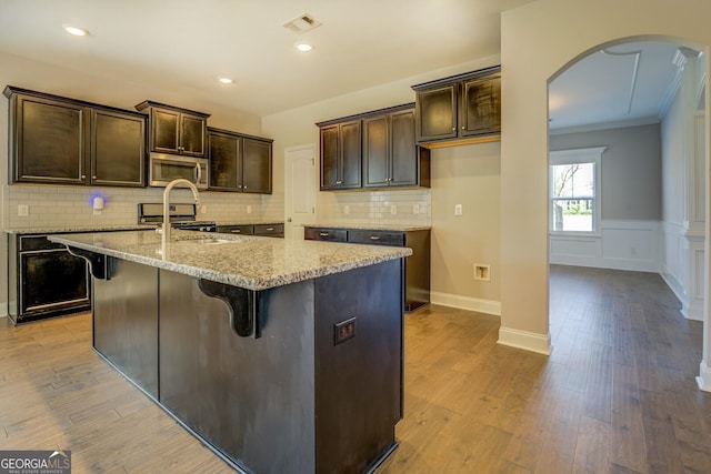 kitchen with dark brown cabinetry, ornamental molding, light stone countertops, stainless steel appliances, and arched walkways