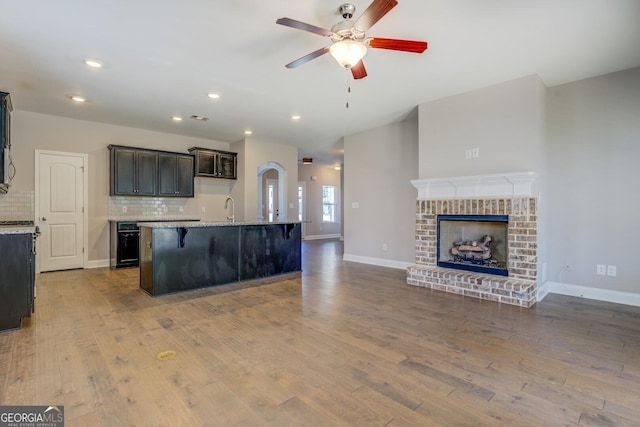 kitchen with open floor plan, a ceiling fan, decorative backsplash, a sink, and wood finished floors