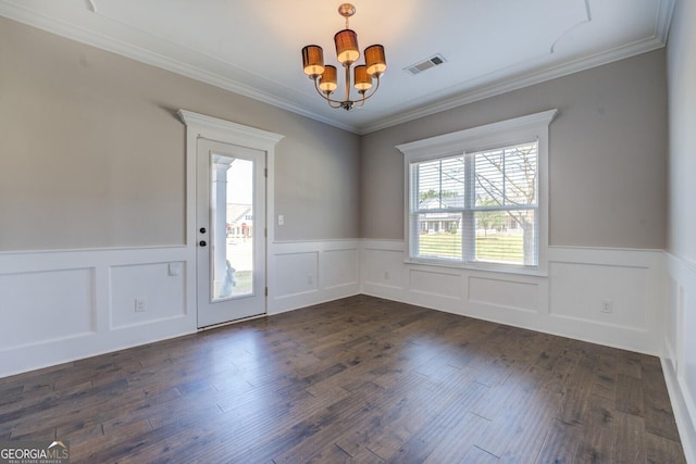 empty room featuring crown molding, dark wood finished floors, visible vents, a wainscoted wall, and a notable chandelier