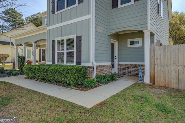 property entrance with board and batten siding, brick siding, fence, and a yard