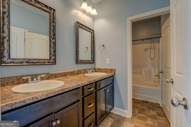 bathroom featuring stone finish floor, double vanity, a sink, and baseboards