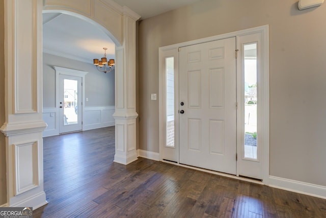 entrance foyer featuring ornamental molding, a chandelier, dark wood-type flooring, ornate columns, and arched walkways