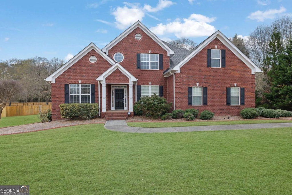 traditional-style home featuring brick siding, fence, and a front lawn