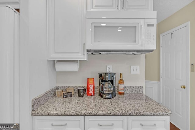 2983 Bancroft Gln NW, Kennesaw, GA 30144 - kitchen featuring white microwave, white cabinetry, light stone countertops, and wainscoting
