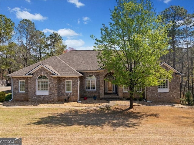 view of front of property featuring brick siding, roof with shingles, and a front lawn