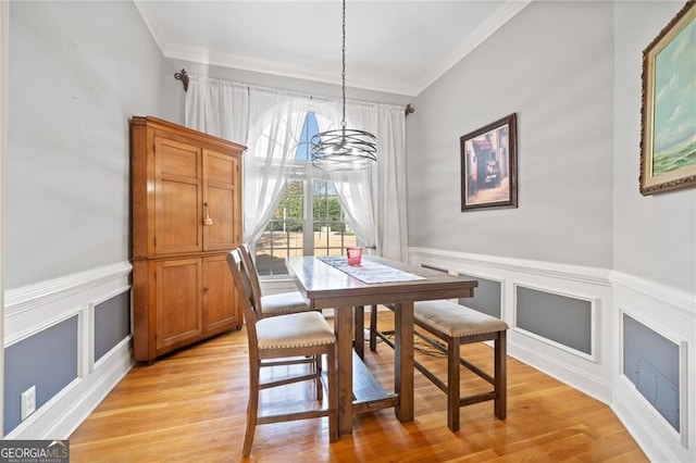 dining area featuring a chandelier, crown molding, a decorative wall, light wood finished floors, and a wainscoted wall