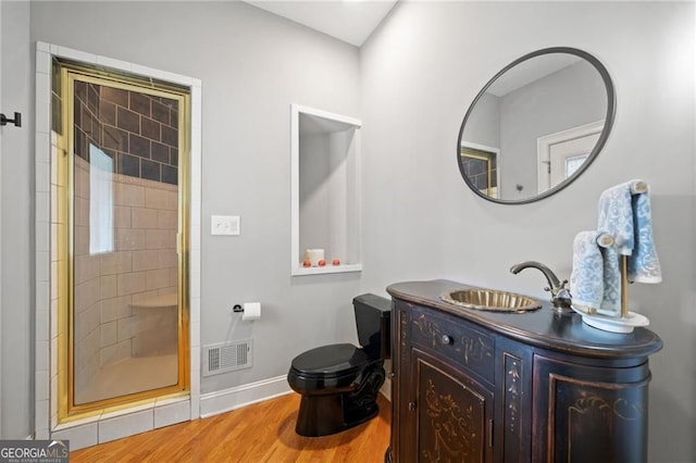 bathroom featuring wood finished floors, toilet, a tile shower, baseboards, and vanity