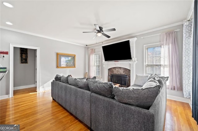 living room featuring ceiling fan, light wood-style floors, a fireplace, baseboards, and crown molding