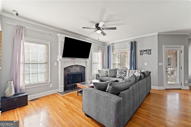living area featuring a ceiling fan, ornamental molding, a premium fireplace, light wood finished floors, and baseboards