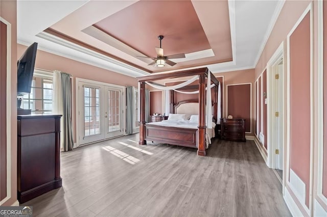 bedroom featuring a raised ceiling, french doors, access to exterior, wood finished floors, and crown molding