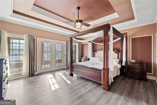 bedroom with a raised ceiling, french doors, access to exterior, ornamental molding, and wood finished floors