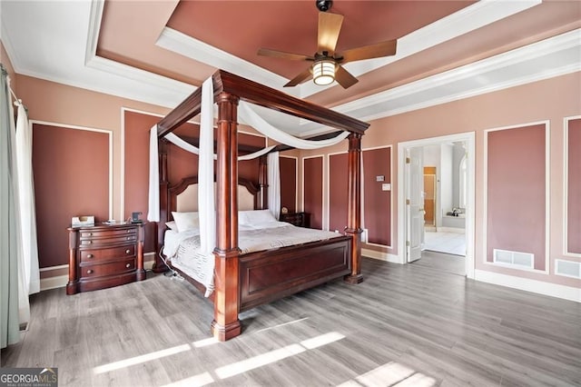bedroom with a tray ceiling, wood finished floors, crown molding, connected bathroom, and baseboards