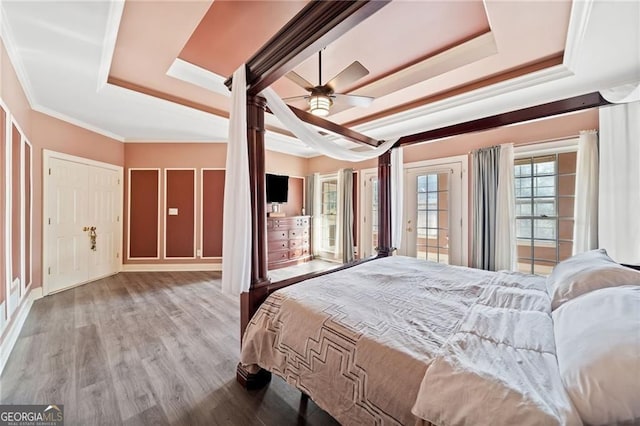 bedroom featuring a tray ceiling, wood finished floors, ornamental molding, access to exterior, and ceiling fan