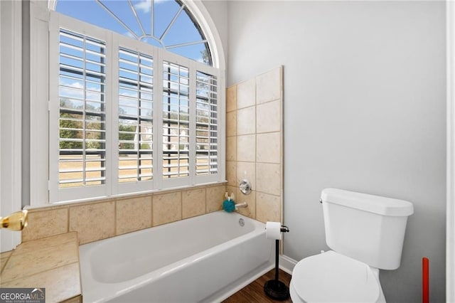 full bath with healthy amount of natural light, toilet, a tub to relax in, and wood finished floors