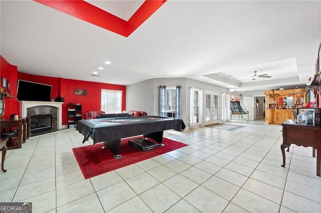 rec room featuring a tray ceiling, light tile patterned flooring, a tile fireplace, ceiling fan, and pool table