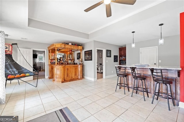interior space featuring light tile patterned floors, ceiling fan, a breakfast bar area, a raised ceiling, and crown molding