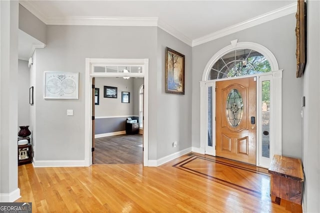 foyer featuring light wood-style floors, crown molding, baseboards, and arched walkways