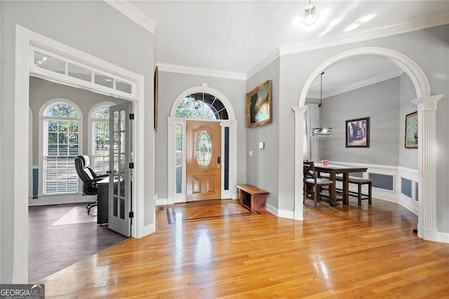 entrance foyer featuring wood finished floors, crown molding, arched walkways, and decorative columns