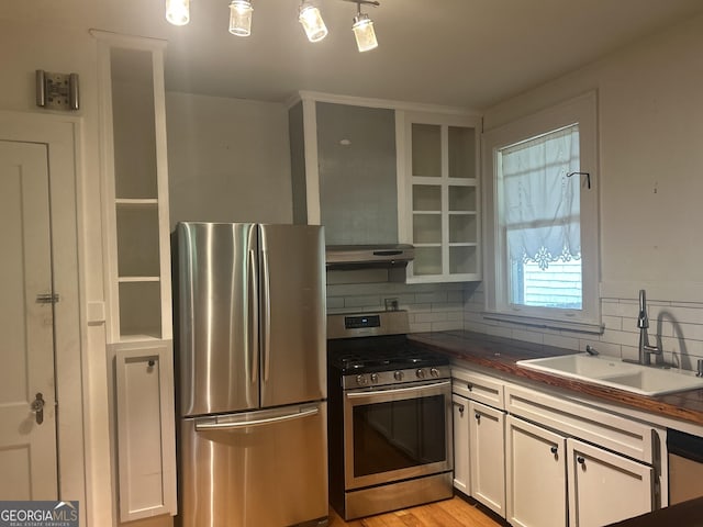 kitchen featuring a sink, range hood, appliances with stainless steel finishes, white cabinets, and decorative backsplash