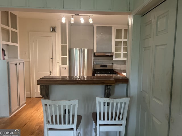 kitchen featuring a peninsula, light wood finished floors, stainless steel appliances, open shelves, and backsplash