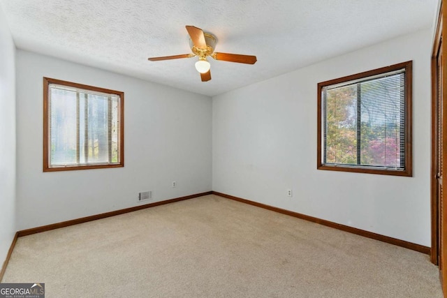 spare room with a textured ceiling, visible vents, baseboards, a ceiling fan, and light colored carpet