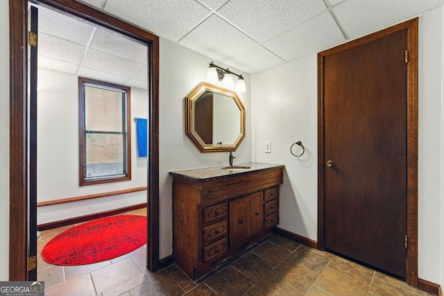 bathroom featuring baseboards, vanity, and a drop ceiling