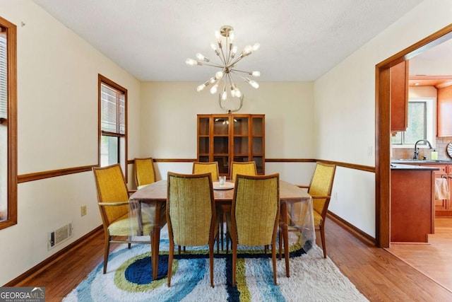 dining space featuring a healthy amount of sunlight, visible vents, a chandelier, and light wood-type flooring