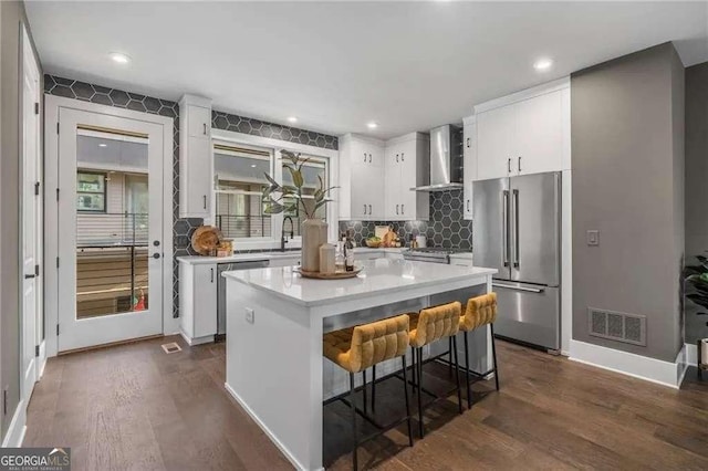 kitchen with wall chimney range hood, high quality fridge, visible vents, light countertops, and dark wood-style floors