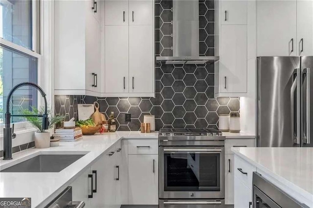 kitchen with white cabinets, a sink, wall chimney range hood, light countertops, and appliances with stainless steel finishes