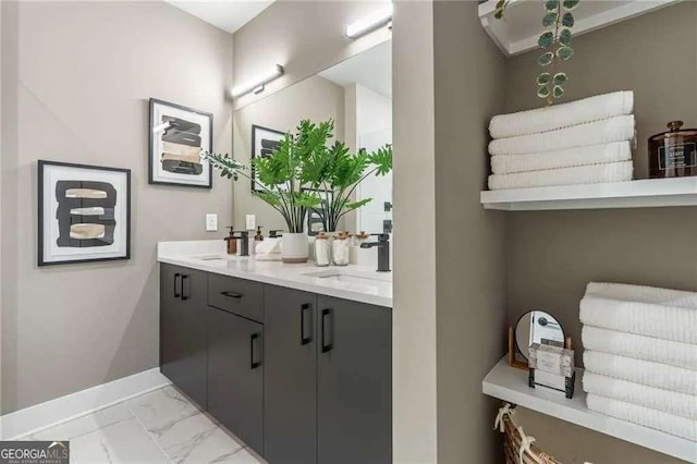 full bath featuring baseboards, double vanity, marble finish floor, and a sink