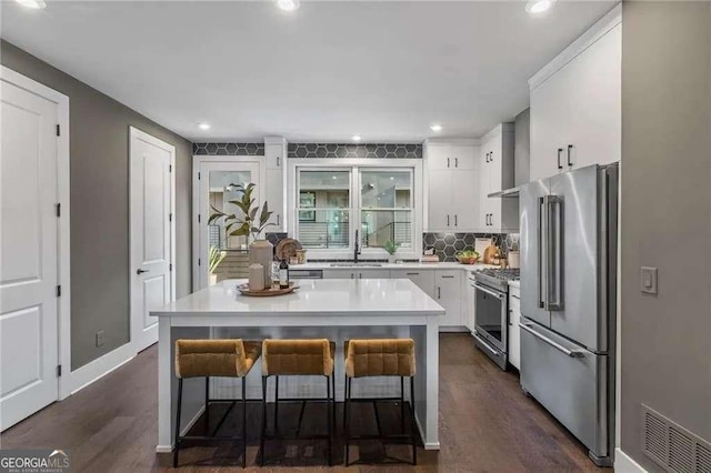 kitchen featuring white cabinetry, light countertops, dark wood-type flooring, a kitchen bar, and premium appliances