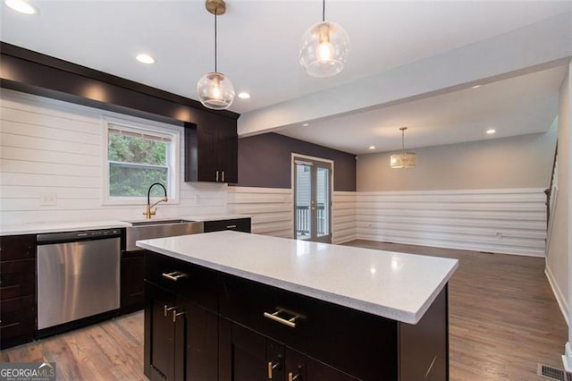 kitchen featuring light countertops, stainless steel dishwasher, hanging light fixtures, a sink, and light wood-style floors
