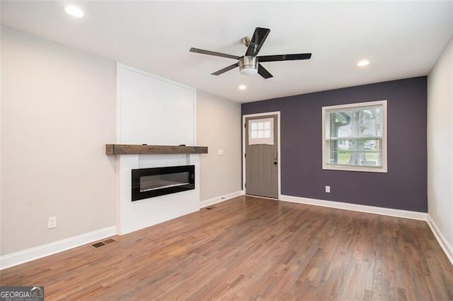 unfurnished living room with visible vents, baseboards, ceiling fan, wood finished floors, and a glass covered fireplace