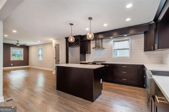 kitchen with wall chimney range hood, light wood finished floors, tasteful backsplash, and a kitchen island