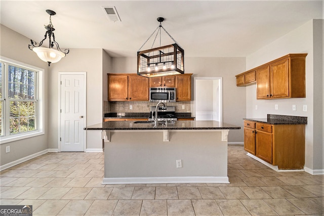 3707 Mcguire St NW, Kennesaw, GA 30144 - kitchen featuring stainless steel microwave, brown cabinetry, backsplash, and light tile patterned floors