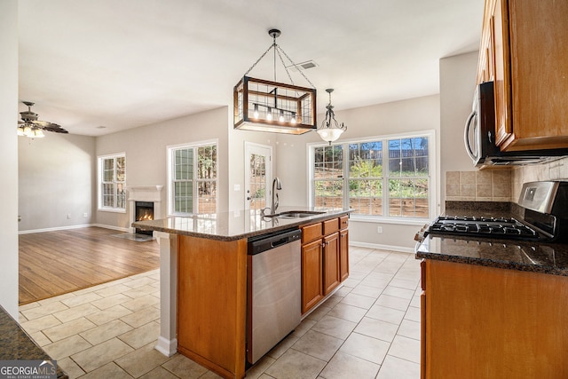 3707 Mcguire St NW, Kennesaw, GA 30144 - kitchen with appliances with stainless steel finishes, a sink, light tile patterned floors, brown cabinets, and a warm lit fireplace